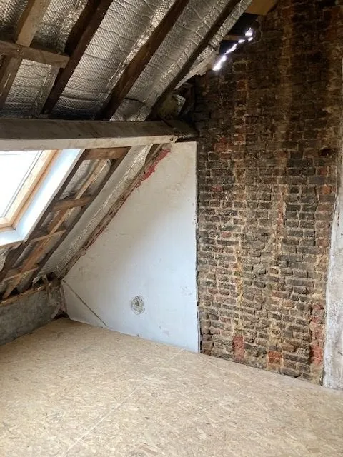 Onafgewerkte zolder met bakstenen muur en dakgebinte vóór de renovatie in Antwerpen